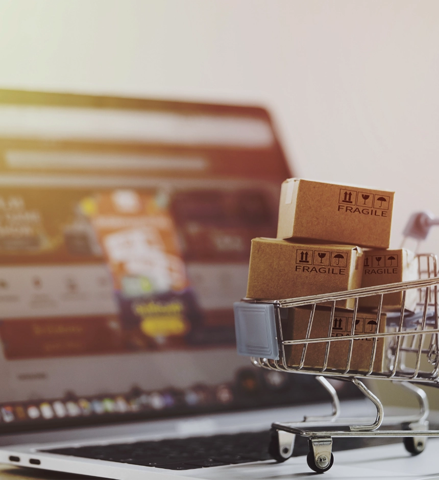 Miniature boxes in a shopping cart in front of a laptop screen.